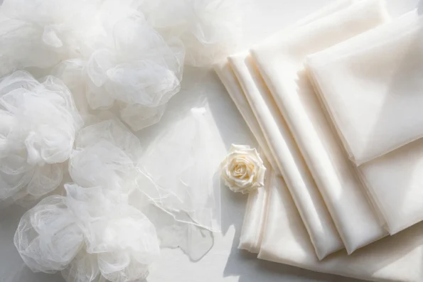 White tulle netting beside folded ivory organza fabric with a white rose