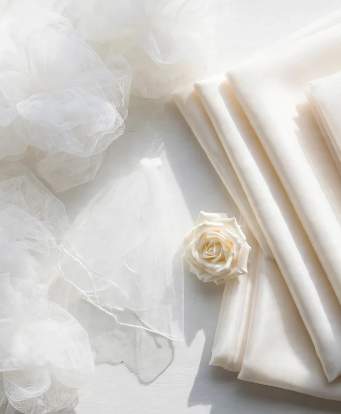 White tulle netting beside folded ivory organza fabric with a white rose